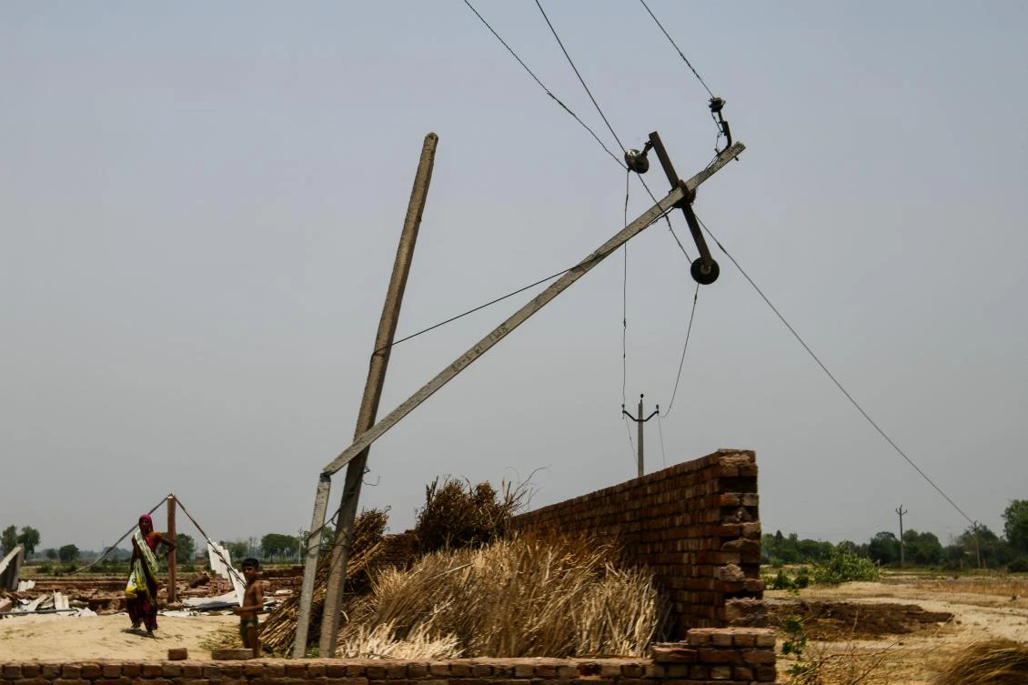 A woman walks past a broken electricity pole caused by heavy storm winds in Kheragarh on the outskirts of Agra. (AFP)