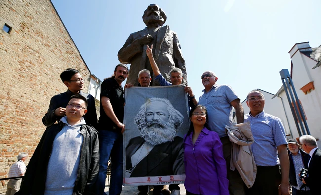 People pose in front of the 4.4 metres (14 feet) high bronze statue of Karl Marx, created by Chinese artist Wu Weishan and donated by China to mark the 200th birth anniversary of the German philosopher, in his hometown Trier, Germany on May 5, 2018. (REUTERS)