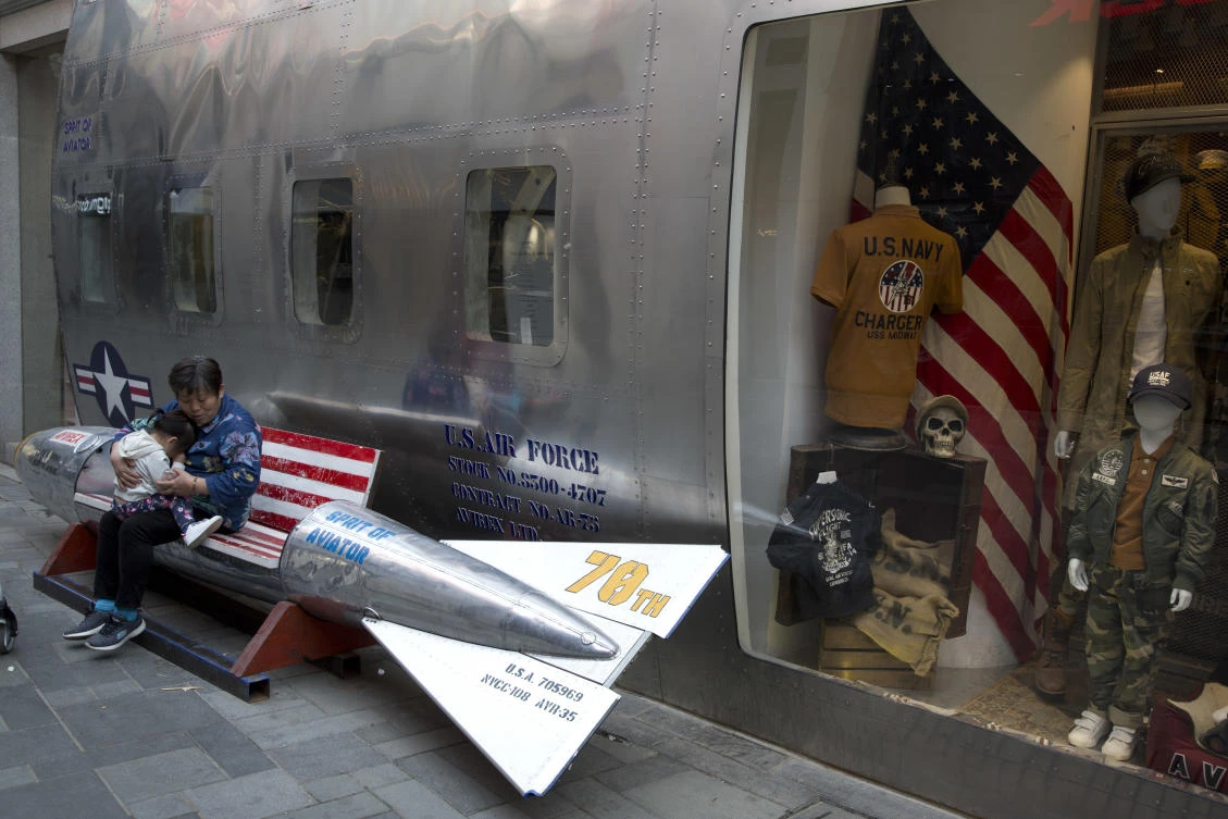A woman tends to a child near a promotional gimmick in the form of a bomb and the US flag outside a US apparel shop in Beijing. China’s lopsided trade balance with the United States means it will run out of imports for retaliation in a trade spat with Washington before President Donald Trump does. (File Photo: AP)