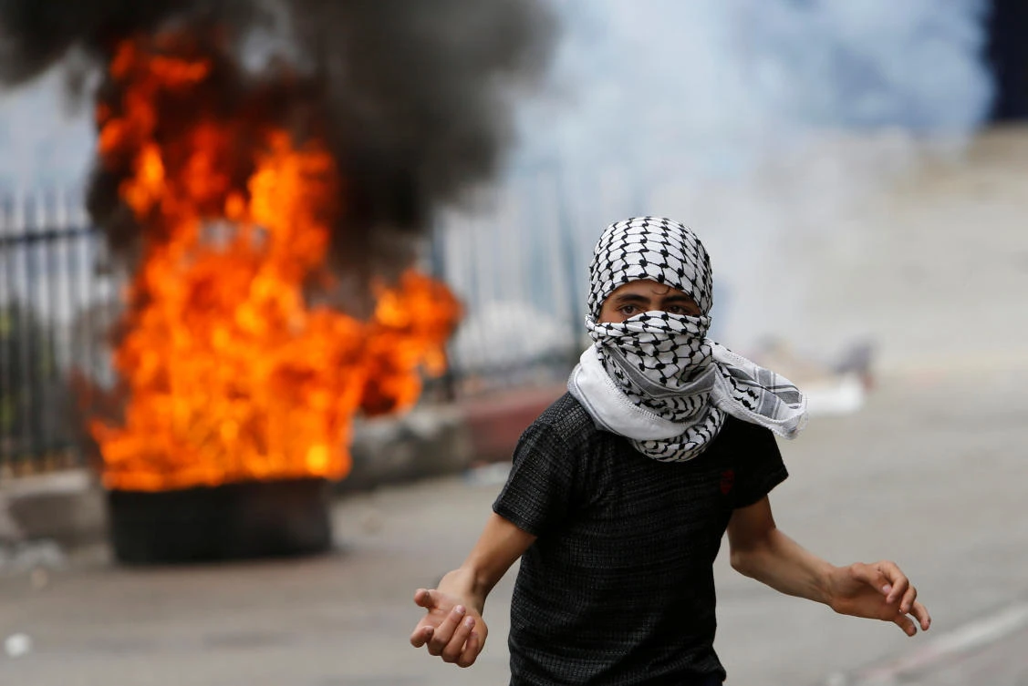 Israeli solider Elor Azaria was initially sentenced to 18 months in prison for the 2016 killing of Abdul Fatah Al-Sharif in the occupied West Bank city of Hebron. Above, a Palestinian protester is seen in front of a burning tire during clashes with Israeli troops in Hebron on May 4. (Reuters)