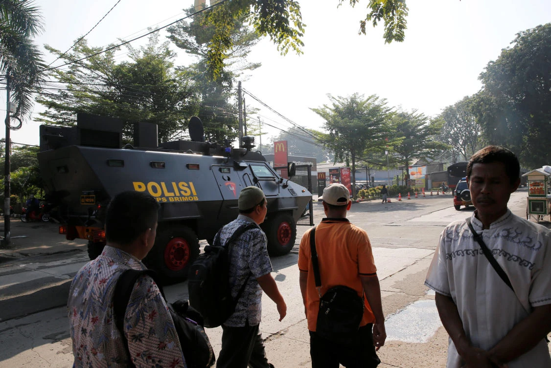 People walk as a police armored vehicle passes a street near Mobile Police Brigade headquarters in Depok, Indonesia where the riots occurred. (Reuters)
