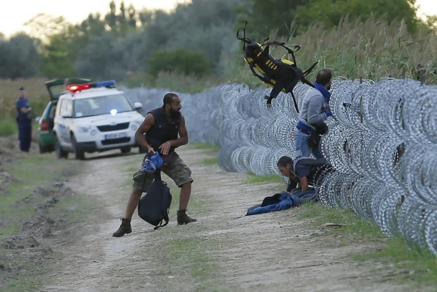 Hungarian police positioned nearby watch as Syrian migrants climb under a fence to enter Hungary at the Hungarian-Serbian border near Roszke. (Reuters)