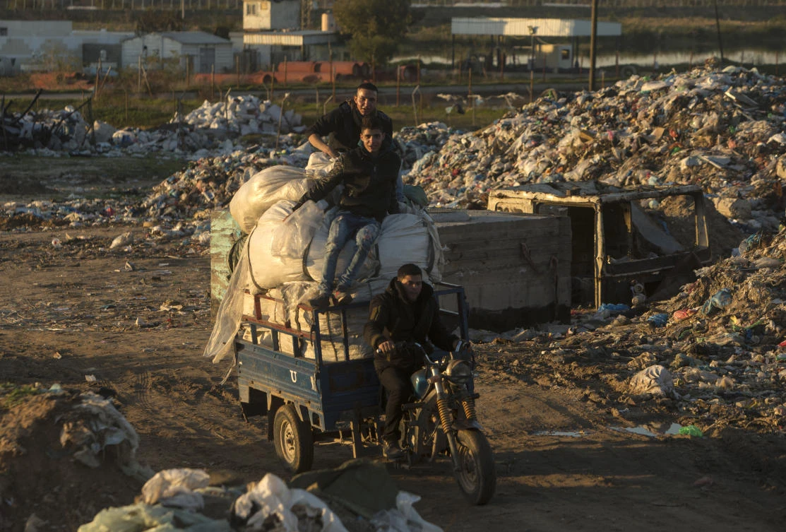 This file image shows Palestinian men on the back of a motor-cart after collecting plastic at a garbage dump (Mahmud Hams/AFP)