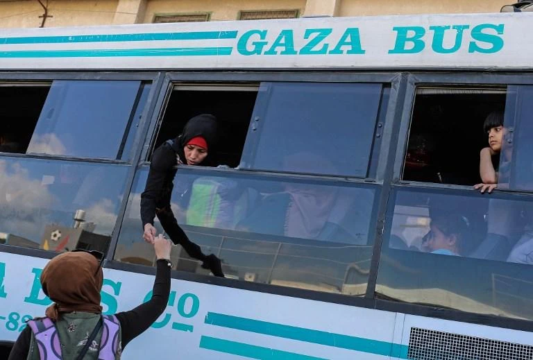 A woman hands an item to a passenger standing in the window of a bus waiting to cross into Egypt from the Rafah border. (AFP)