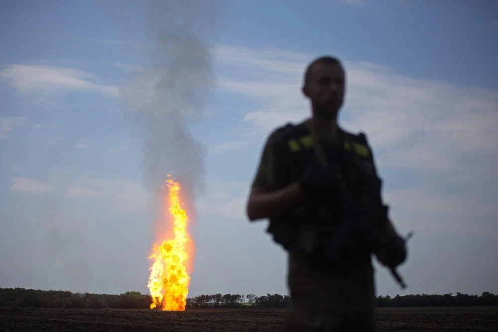 A Ukrainian serviceman stands guard, as flames erupt in the distance from a gas pipeline that was damaged as a result of shelling by pro-Russian separatists, near Avdiivka, Donetsk region, on June 12, 2015. (AFP)