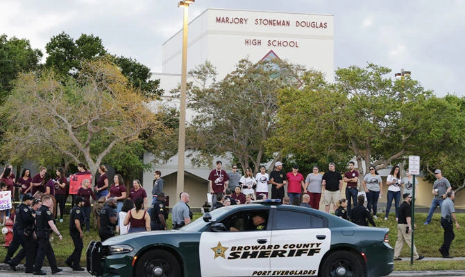In this Feb. 28, 2018 file photo, a police car drives near Marjory Stoneman Douglas High School in Parkland, Florida, as students return to class for the first time since a former student opened fire there with an assault weapon. (AP Photo/Terry Renna)