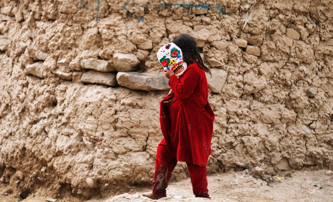 An internally-displaced Afghan girl holds a mask as she walks outside a shelter at a refugee camp in Kabul, Afghanistan on Monday. (REUTERS)