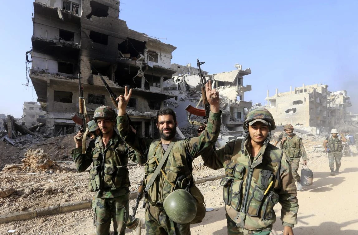 Syrian government forces gesture as they walk down a destroyed street in the Palestinian camp of Yarmuk on the southern outskirts of Damascus. (AFP)