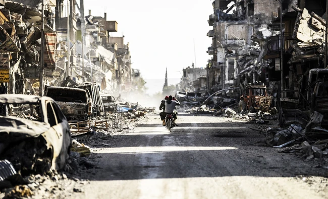 A Syrian youth uses his cell phone to film the destroyed vehicles and heavily damaged buildings down a street in Raqa. Files/ AFP