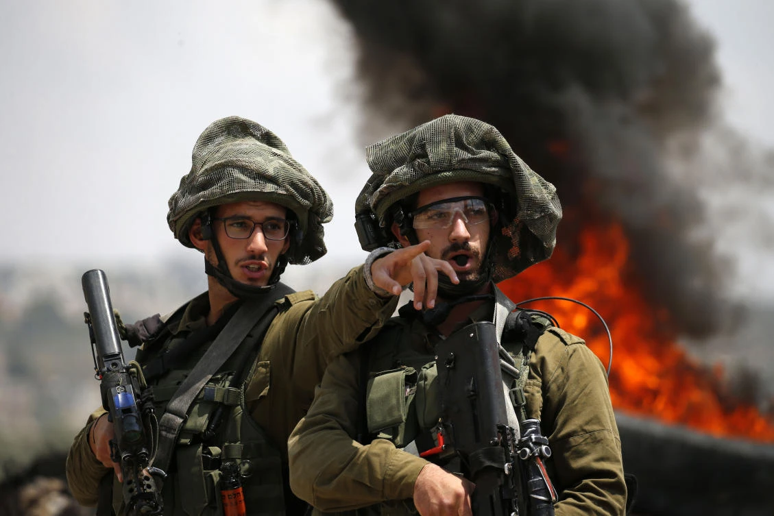 File photo showing 2 Israeli soldiers talking while demonstration against the expropriation of Palestinian land by Israel in the village of Kfar Qaddum, near Nablus in the occupied West Bank, June 1, 2018. (AFP)