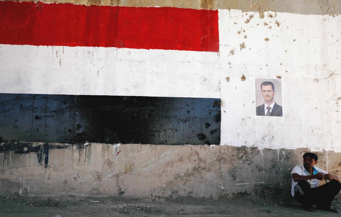 A man sits near a poster of Syrian President Bashar al Assad during the re-opening of the road between Homs and Hama in Talbisi, Syria June 6, 2018. (Reuters)