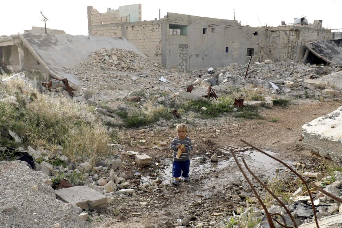 File photo shows a Syrian child eating among destroyed buildings in Kobani on May 27, 2018. (AFP)