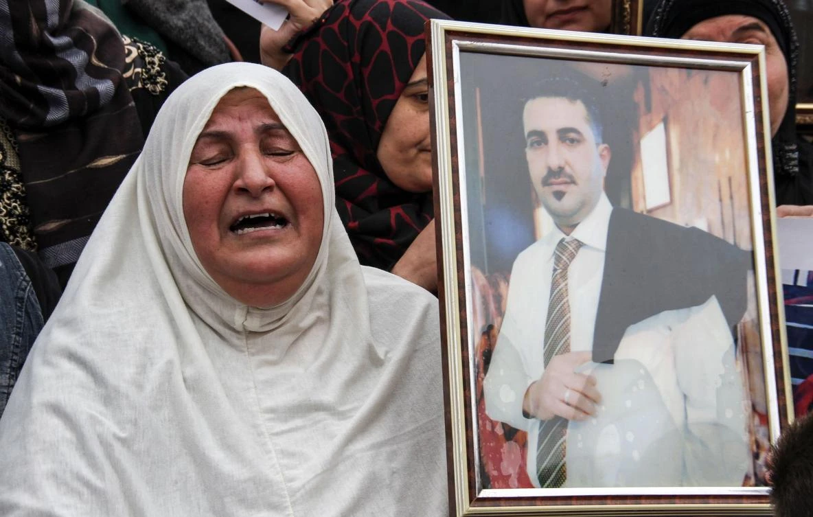 A woman holds up a portrait of a missing relative, who was held captive by Daesh fighters, during a demonstration in Mosul’s Al-Minassa Square. (AFP)