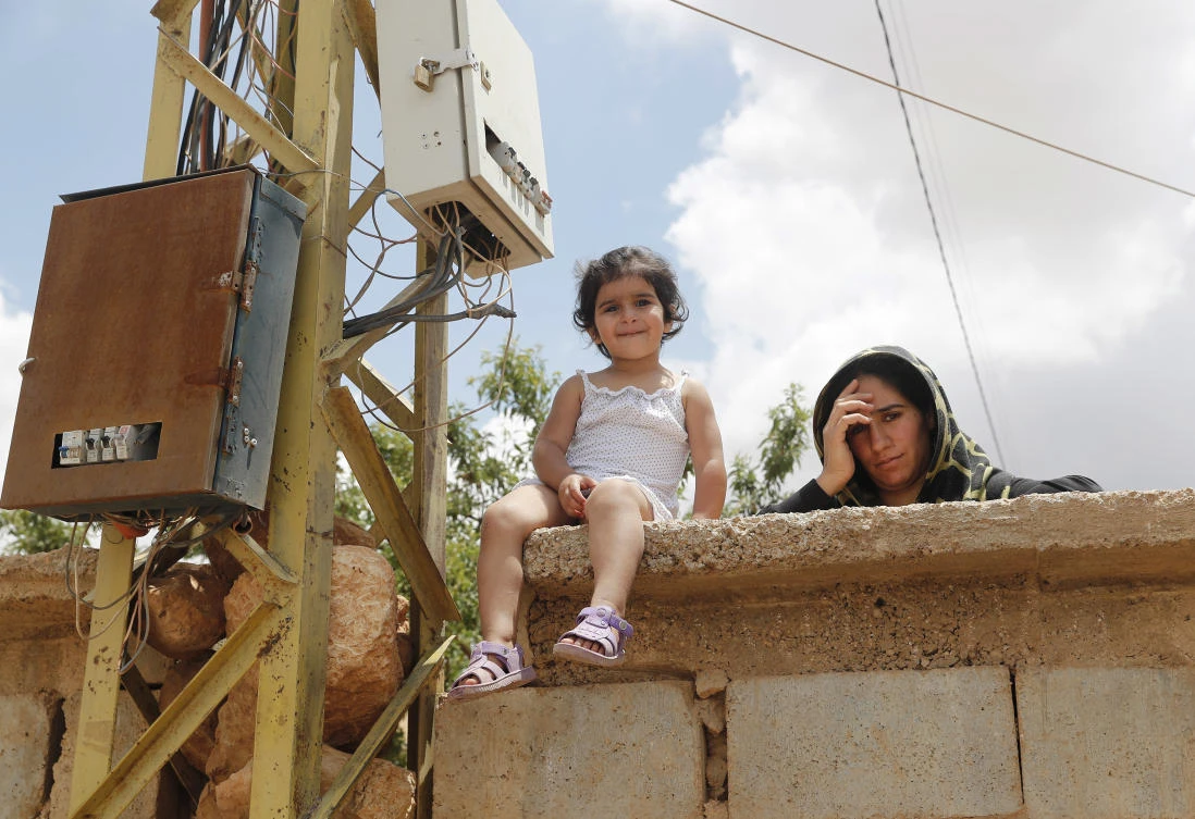 A Syrian refugee woman stands next to her daughter as she watches the visit of the Lebanese Foreign Minister Gibran Bassil to their refugee camp, in Arsal, near the border with Syria, east Lebanon, Wednesday, June 13, 2018. (AP)