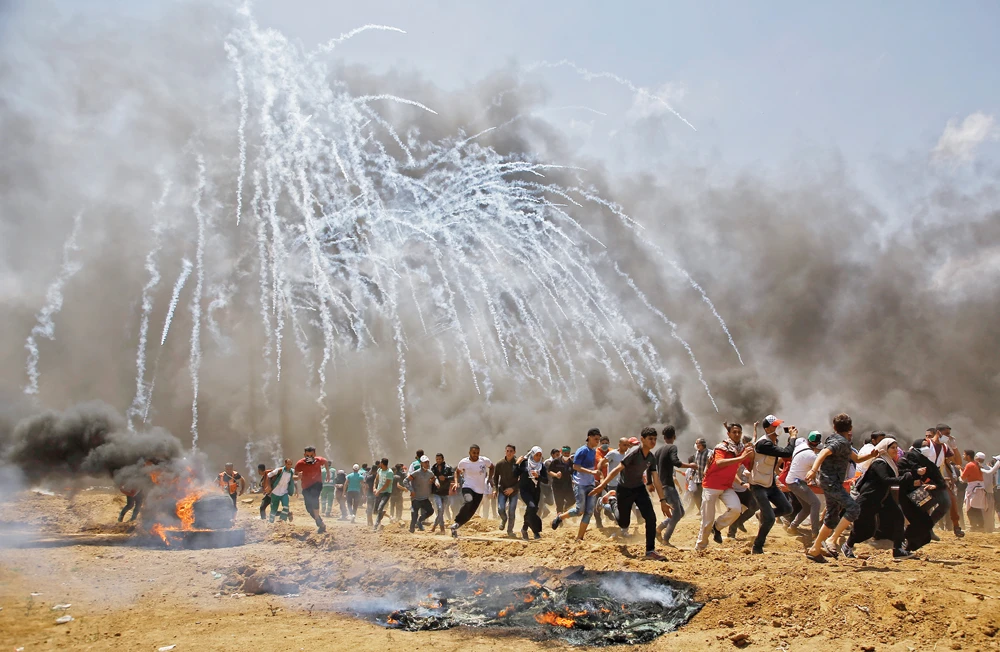 Palestinians run for cover from tear gas during clashes with Israeli security forces near the border between Israel and the Gaza Strip, east of Jabalia, on May 14. (AFP/File)