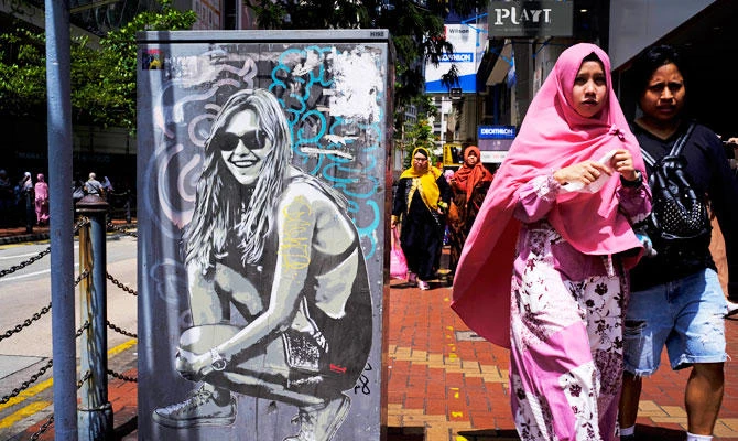 An Indonesian resident walks past graffiti on a down town street in Hong Kong Sunday, June 17, 2018. (AP)