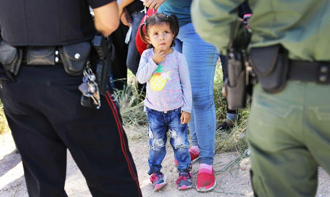 A Mission Police Dept. officer (L), and a US Border Patrol agent watch over a group of Central American asylum seekers before taking them into custody on June 12, 2018 near McAllen, Texas. (AFP)