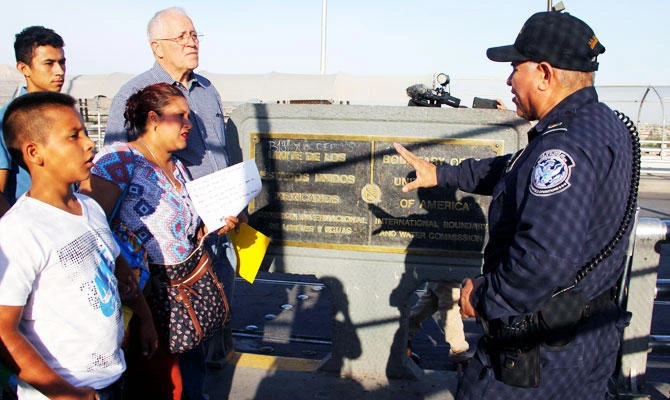 A Customs and Border Protection Agent talks to US activist Ricardo Garcia (C) from Casa Asuncion shelter, after stopping a group of Honduran and Guatemalan migrants who arrived to ask for political asylum in US, at the Paso del Norte International Bridge, in Ciudad Juarez Chihuahua, Mexico on the border with El Paso, Texas, US, on June 15, 2018. (AFP)