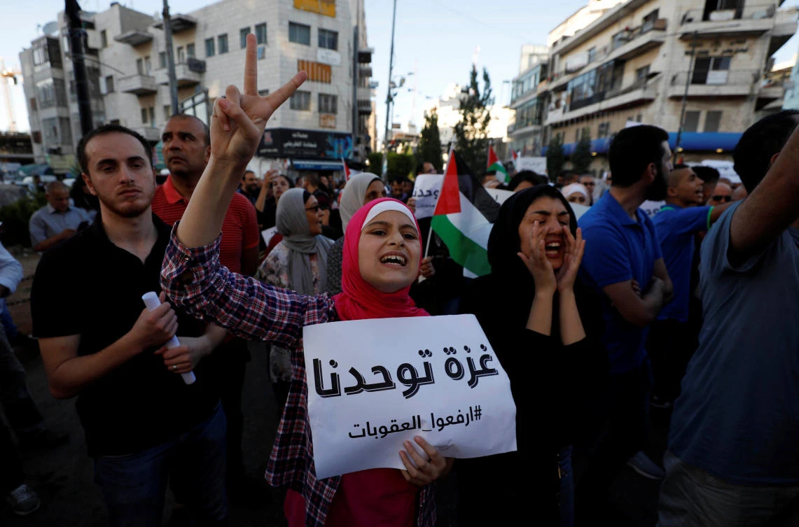A Palestinian woman gestures as she holds a sign that reads "Gaza unites us" during a protest calling on President Mahmoud Abbas to lift the sanctions on Gaza Strip, in Ramallah, in the occupied West Bank, June 23, 2018. (Reuters)