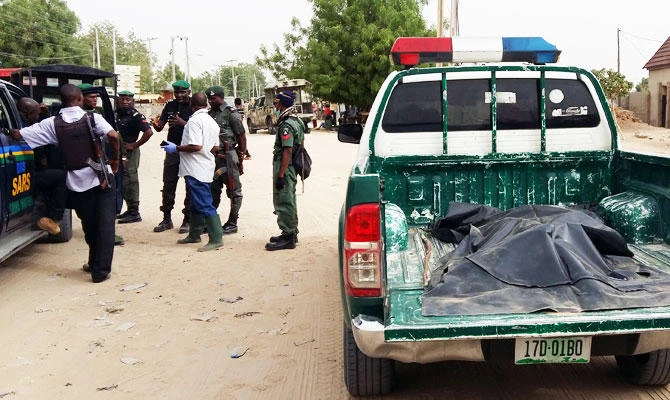 A covered-up dead body lies in the trunk of a police vehicle as members of security forces stand near the site of a suspected Boko Haram attack on the edge of Maiduguri's inner city, Nigeria April 2, 2018. (REUTERS)