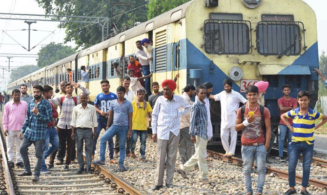 Indian passengers stand next to train carriages during a protest along train tracks by Indian farmers against the central and state governments for not implementing their demands, at the Manawala railway station, on September 29, 2017. (AFP)