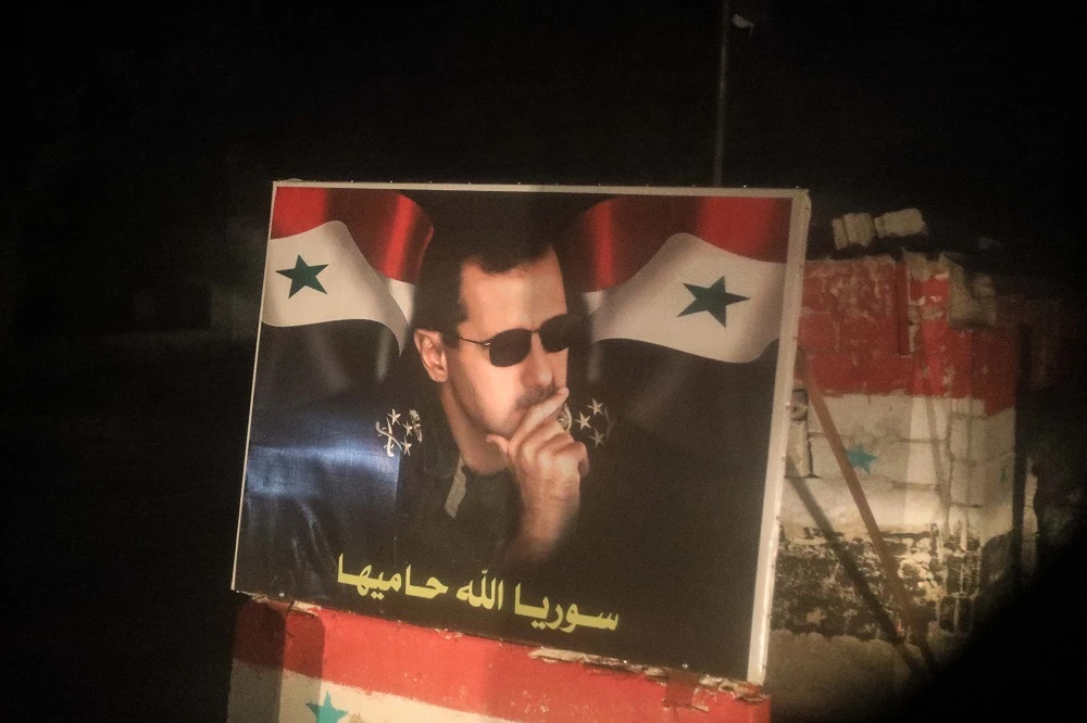 A picture taken through a window of a bus carrying Syrian civilians and rebel-fighters from the town of Douma shows a poster of President Bashar al-Assad at a checkpoint in the city of Tartus, on April 2, 2018. (File photo: AFP)