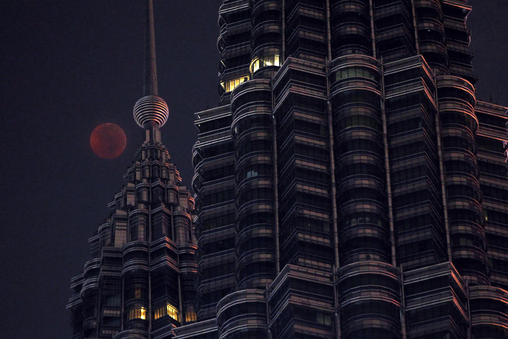 A full moon sets over Petronas Twin Tower during a complete lunar eclipse in Kuala Lumpur, Malaysia, on July 28, 2018. (AP Photo/Yam G-Jun)