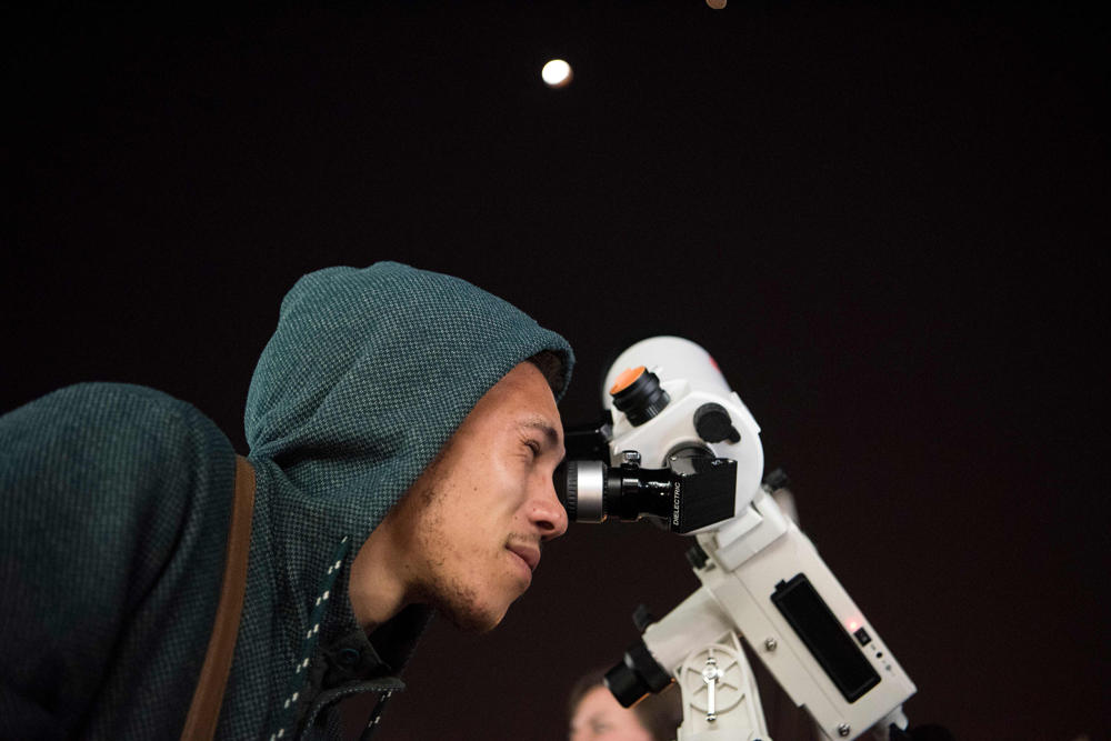 A man looks through a telescope at the full moon during a "blood moon" eclipse in from Cape Town on July 27, 2018. (AFP / RODGER BOSCH)
