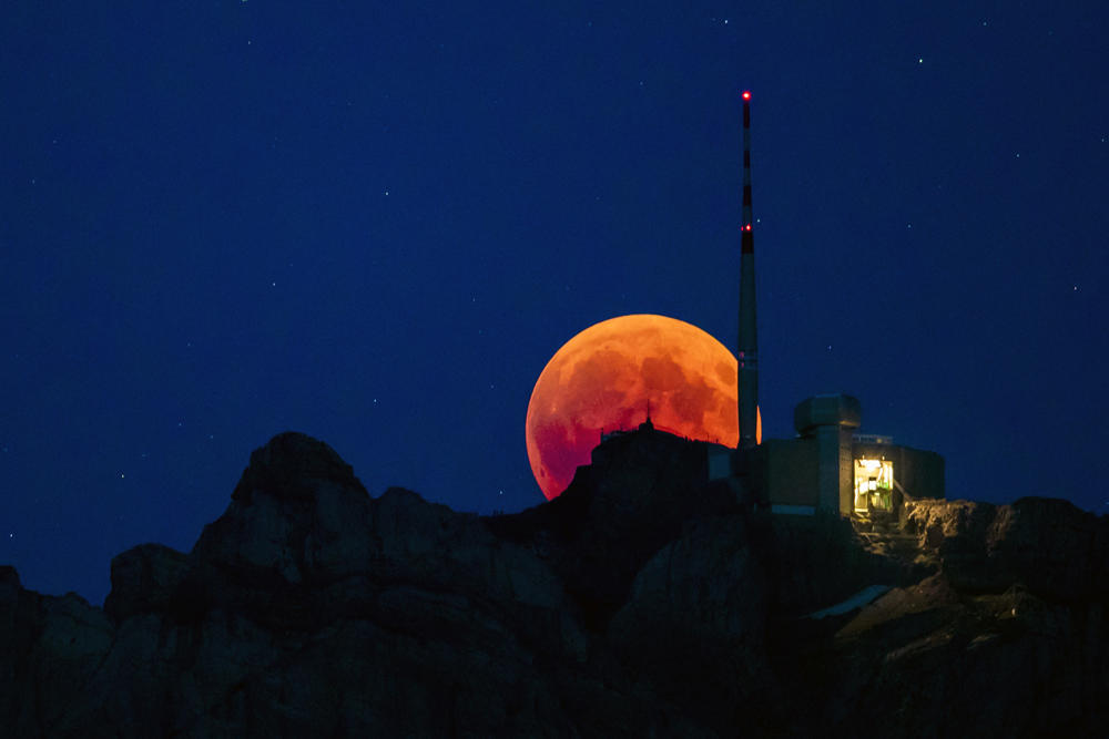 The moon turns red during a total lunar eclipse, behind the Saentis in Luzern, Switzerland, on July 27, 2018. (Christian Merz/Keystone via AP)