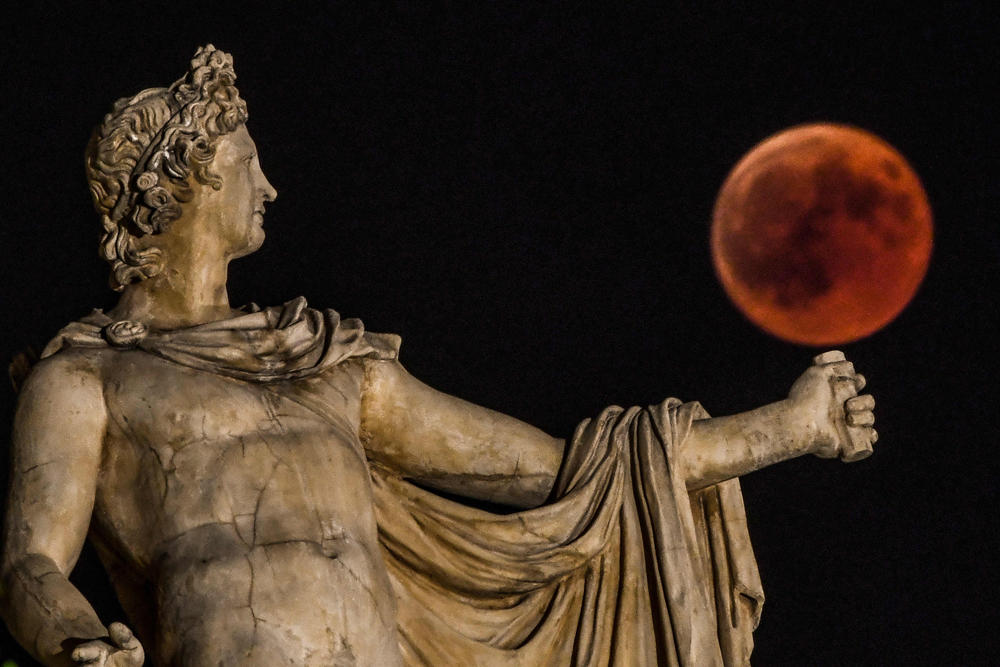 A picture shows the full moon during a "blood moon" eclipse beside a statue of the ancient Greek god Apollo in central Athens on July 27, 2018. (AFP / Aris Messinis)