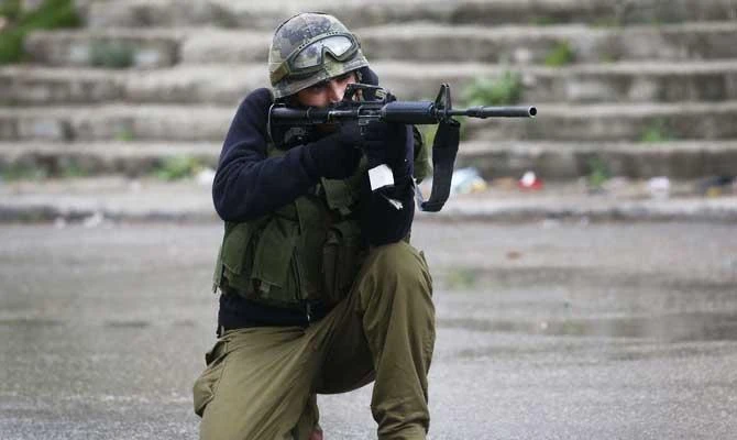 An Israeli soldier aims his gun during clashes with Palestinian protestors following the funeral of Hamza Zamareh in the village of Halhul, north of the occupied West Bank city of Hebron, on February 17, 2018. (AFP)