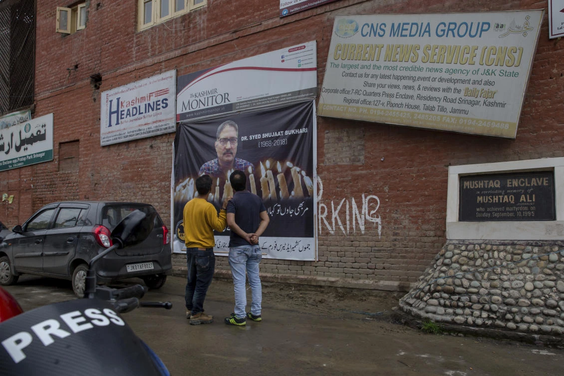 Kashmiri men look at the poster displaying the picture of slain journalist Shujat Bukhari in Srinagar on Wednesday, July 4. Reporters Without Borders said in a report that four journalists in India were killed in the first six months of the year. (AP)