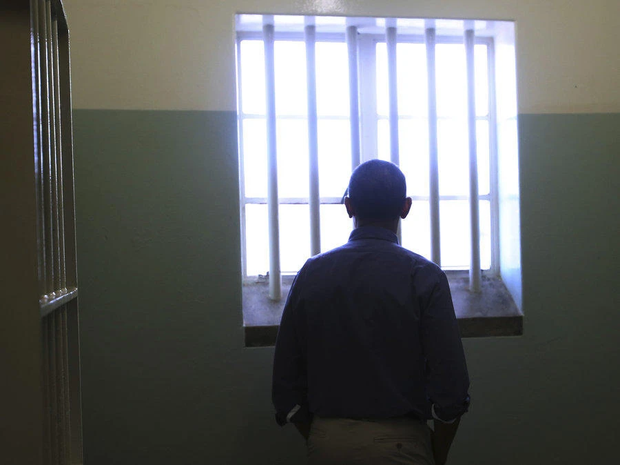 Barack Obama looks out the window of the Robben Island prison cell that once held Nelson Mandela. A night in his iconic 8-foot by 7-foot (2.4 meters by 2.1 meters) concrete cell will now be auctioned for charity to mark the centenary of prisoner number 46664’s birthday. (Reuters)