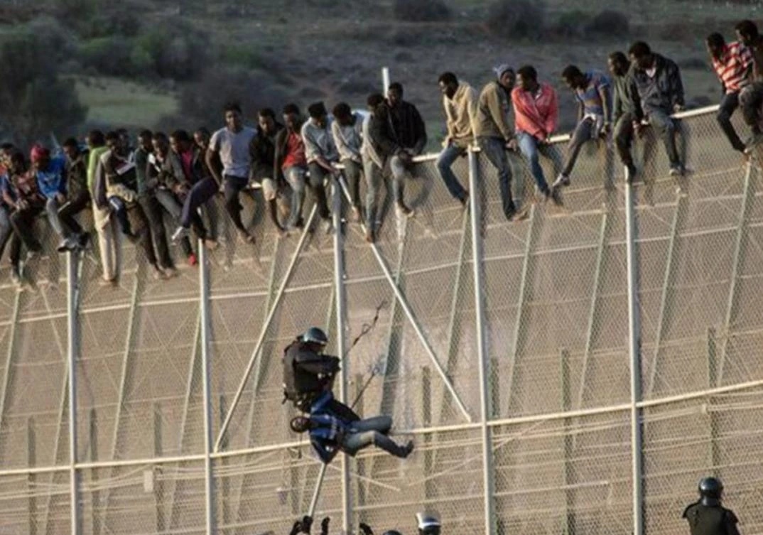 Immigrants attempting to scale a barbed-wire fence that juts into the sea. (File photo: Reuters)