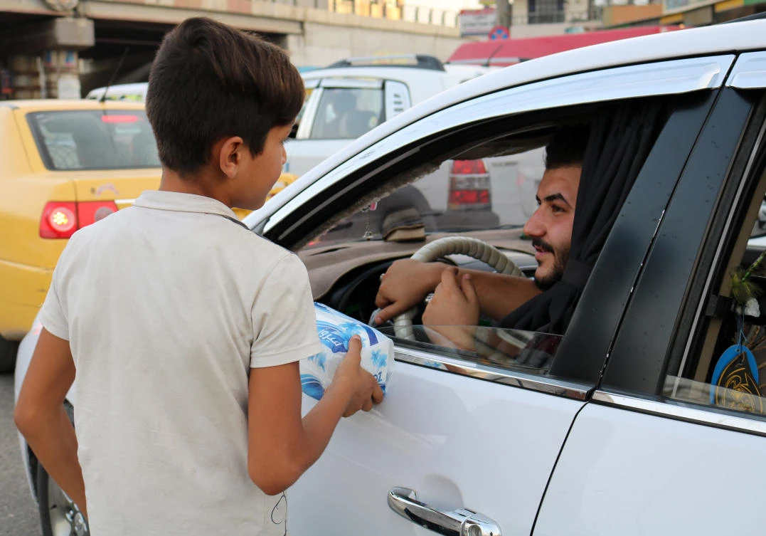 An Iraqi child peddlar sells tissue paper to cars driving down a street in the northern Iraqi city of Mosul on July 7, 2018. (AFP)