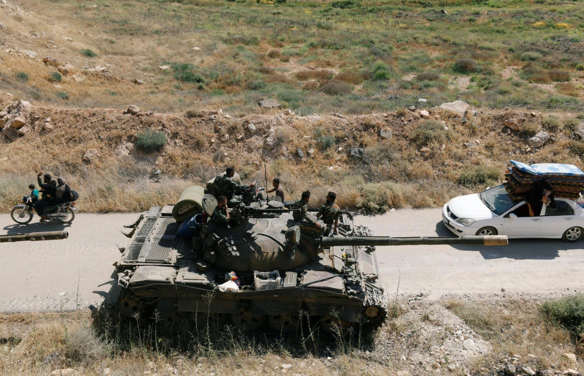 Civilians pass by a Syrian forces’ tank of President Bashar Assad in Daraa on Satuday, July 7. (Reuters)