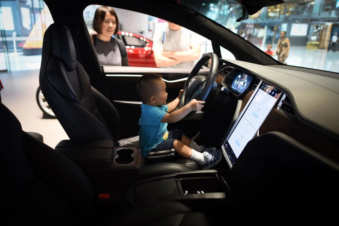 A boy sits in a Tesla car during a visit at Tesla showroom in Beijing on July 4, 2018. (AFP)