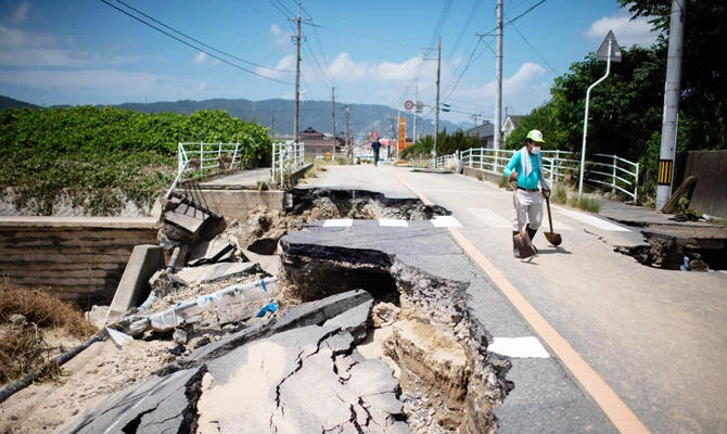 A man with a showel walks on a damaged road in a flood hit area in Mabi, Okayama prefecture on July 10, 2018. (AFP)