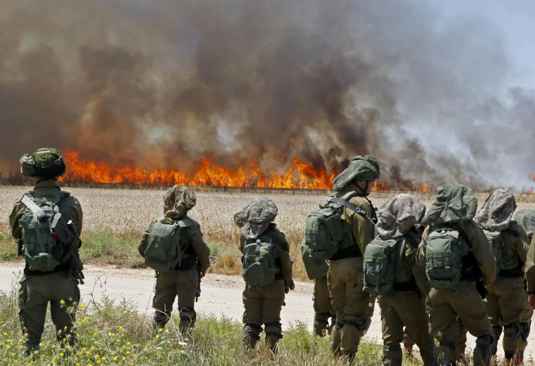 Israeli soldiers face the smoke from a fire caused by incendiaries tied to kites flown by Palestinian protesters. (File/AFP)