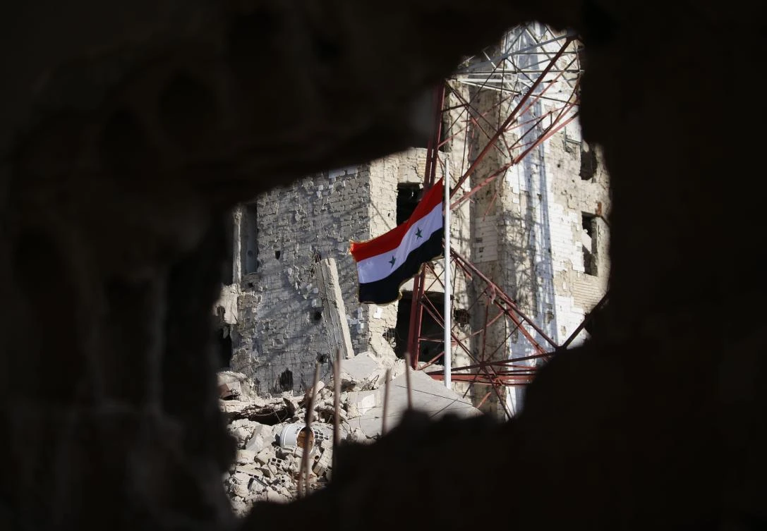 The Syrian national flag rises in the midst of damaged buildings in Daraa-al-Balad, an opposition-held part of the southern city of Daraa, on July 12, 2018. (File Photo: AFP/Mohamad Abazeed)