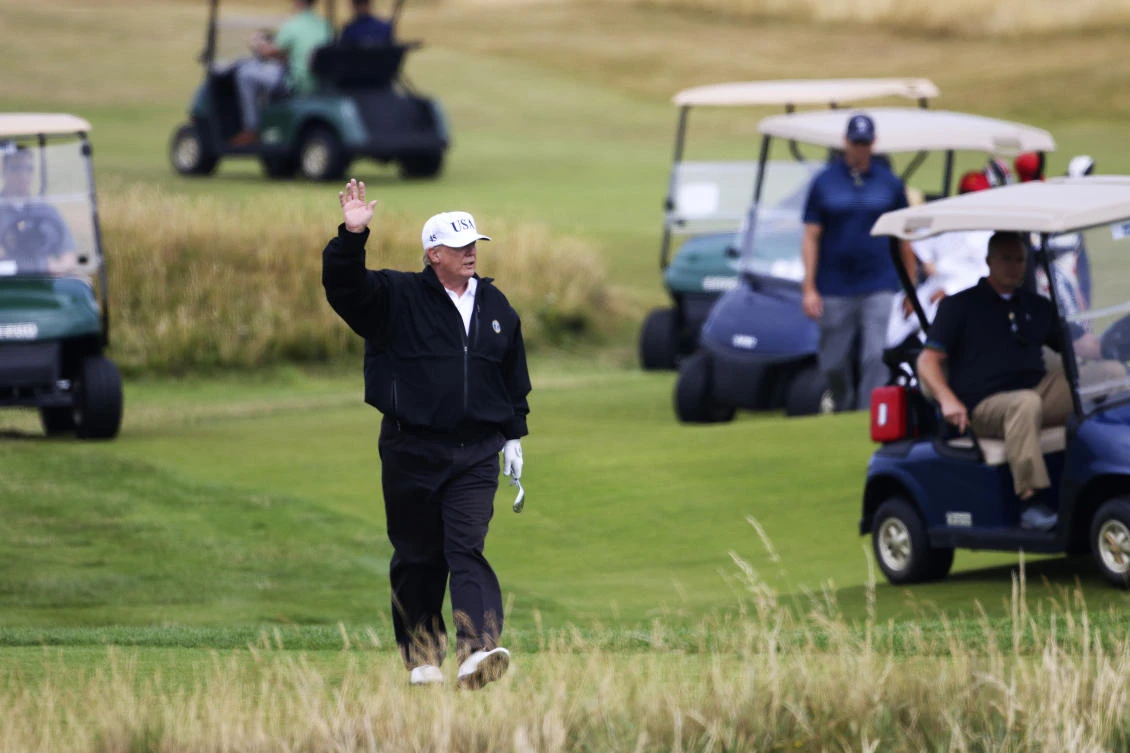 US President Donald Trump waves to protesters while playing golf at Turnberry golf club, in Turnberry, Scotland, Saturday, July 14, 2018. (AP)