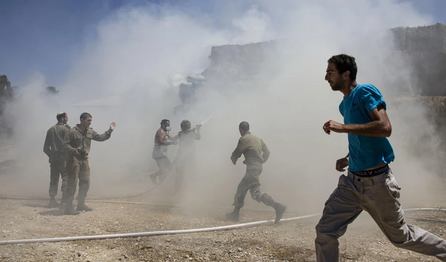 Israeli firefighters and soldiers attempt to extinguish a fire next to a cow shed, caused by a incendiary balloon launched by Palestinians from the Gaza Strip on July 21, 2018. (AP Photo/Tsafrir Abayov)