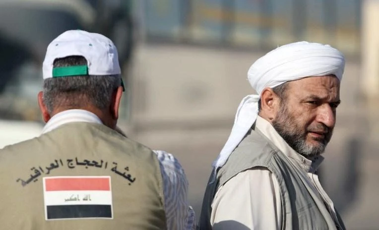 In this file photo, an Iraqi tour guide (L) wearing a waistcoat with the Iraqi flag and written in Arabic, "Iraqi Pilgrims" stands on hand as his clients go through passport control at the Arar southern Iraqi border crossing with Saudi Arabia. (AFP)