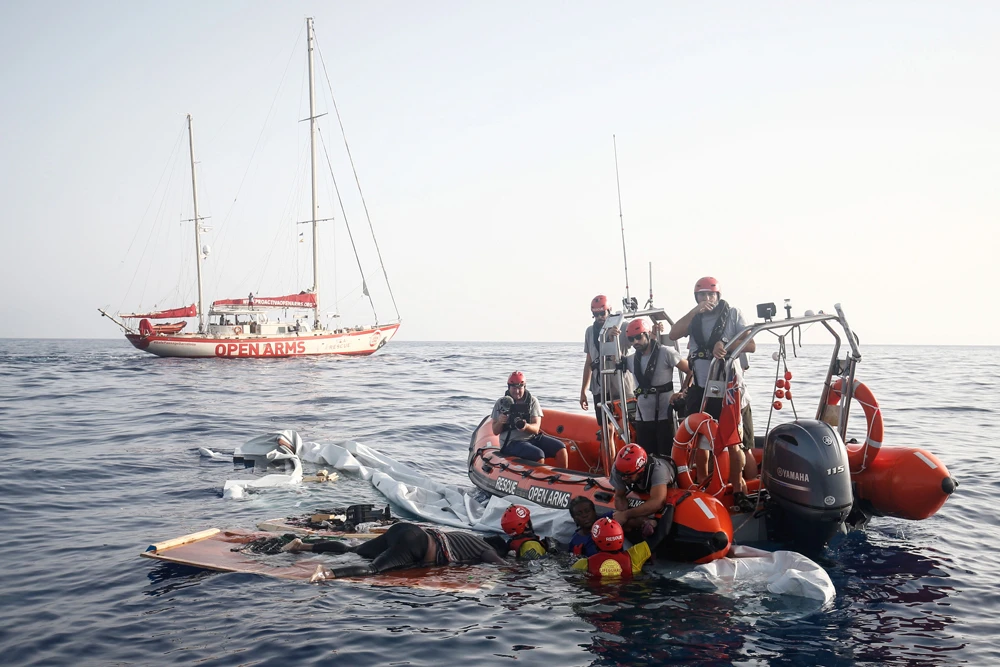 Members of the Spanish NGO Proactiva Open Arms' lift a woman out of the water as another lies dead on the remains of the sunken boat in the Mediterranean Sea about 85 miles off the Libyan coast on July 17, 2018. (AFP / PAU BARRENA)