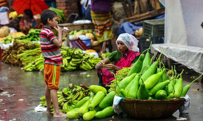 A Bangladeshi street vendor and child wait for customers in the rain at a market in Dhaka on July 24, 2018. (AFP)