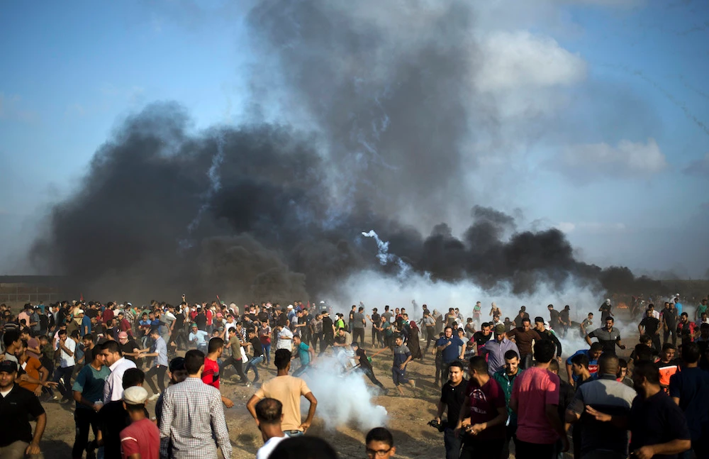 Palestinian protesters escape from teargas fired by Israeli troops during a protest at the Gaza Strip's border with Israel, Friday, Aug. 3, 2018. (AP)