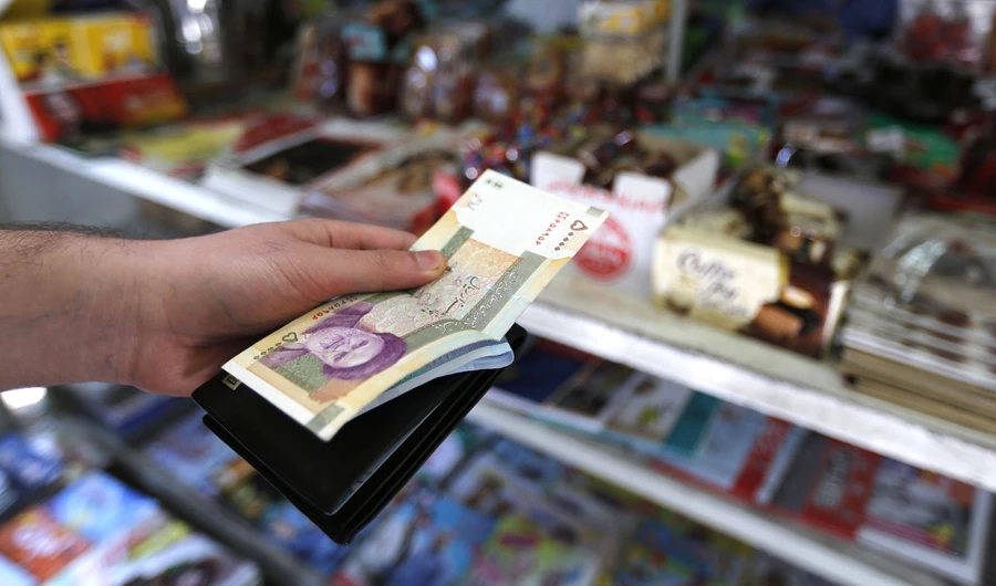 A man holds a stack of Iranian Rials in front of a shop in Tehran on July 31, 2018. (AFP / ATTA KENARE)