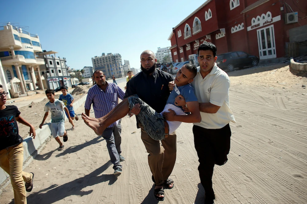 Palestinian employees of Gaza City’s Al-Deira hotel carry a wounded boy following an Israeli military strike nearby on the beach, on July 16, 2014. (AFP)