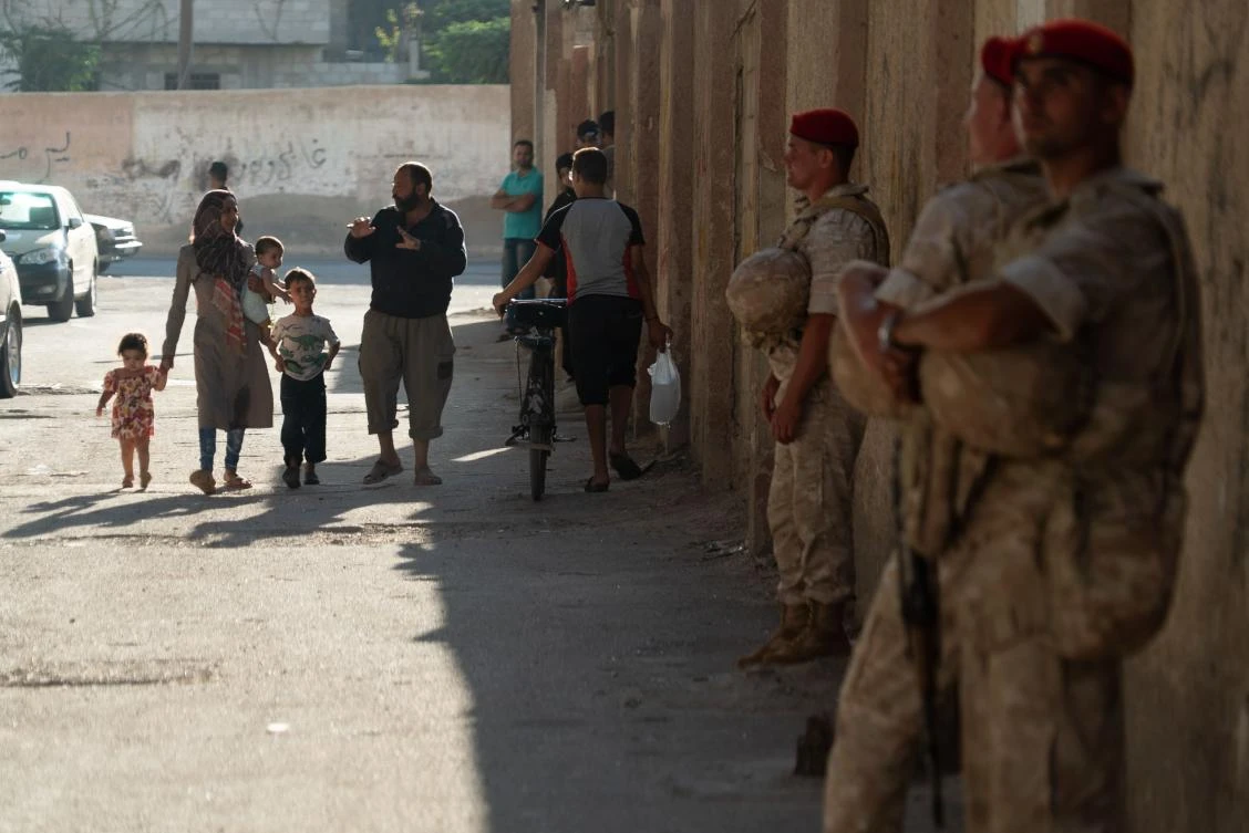 Syrian civilians walk past Russian military personnel on August 13, 2018 in Yalda, in the southern suburbs of the capital Damascus, during a guided tour with the Russian army. (AFP)