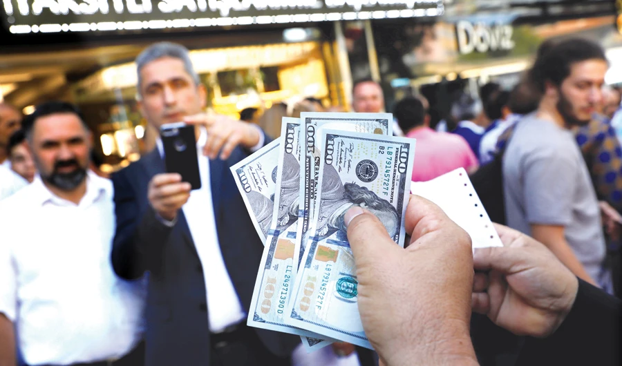 A businessman holding US dollars poses for his friend in front of a currency exchange office in Ankara. (Reuters)